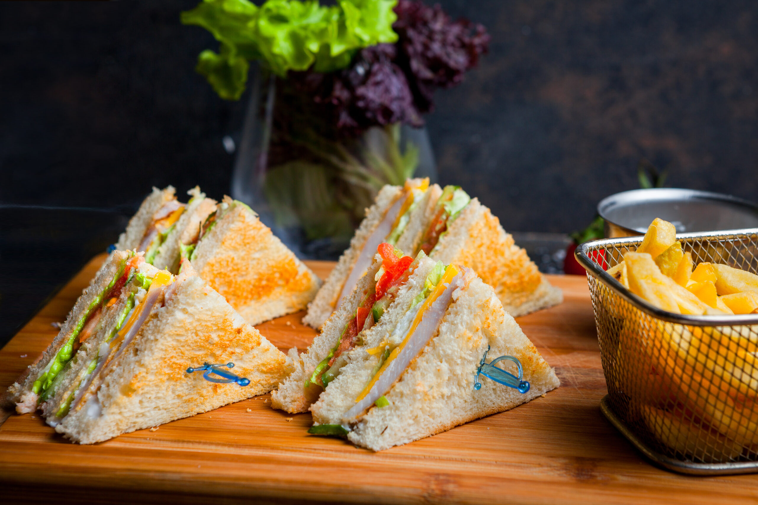 Side view club sandwich with french fries in wooden serving board on dark stone background